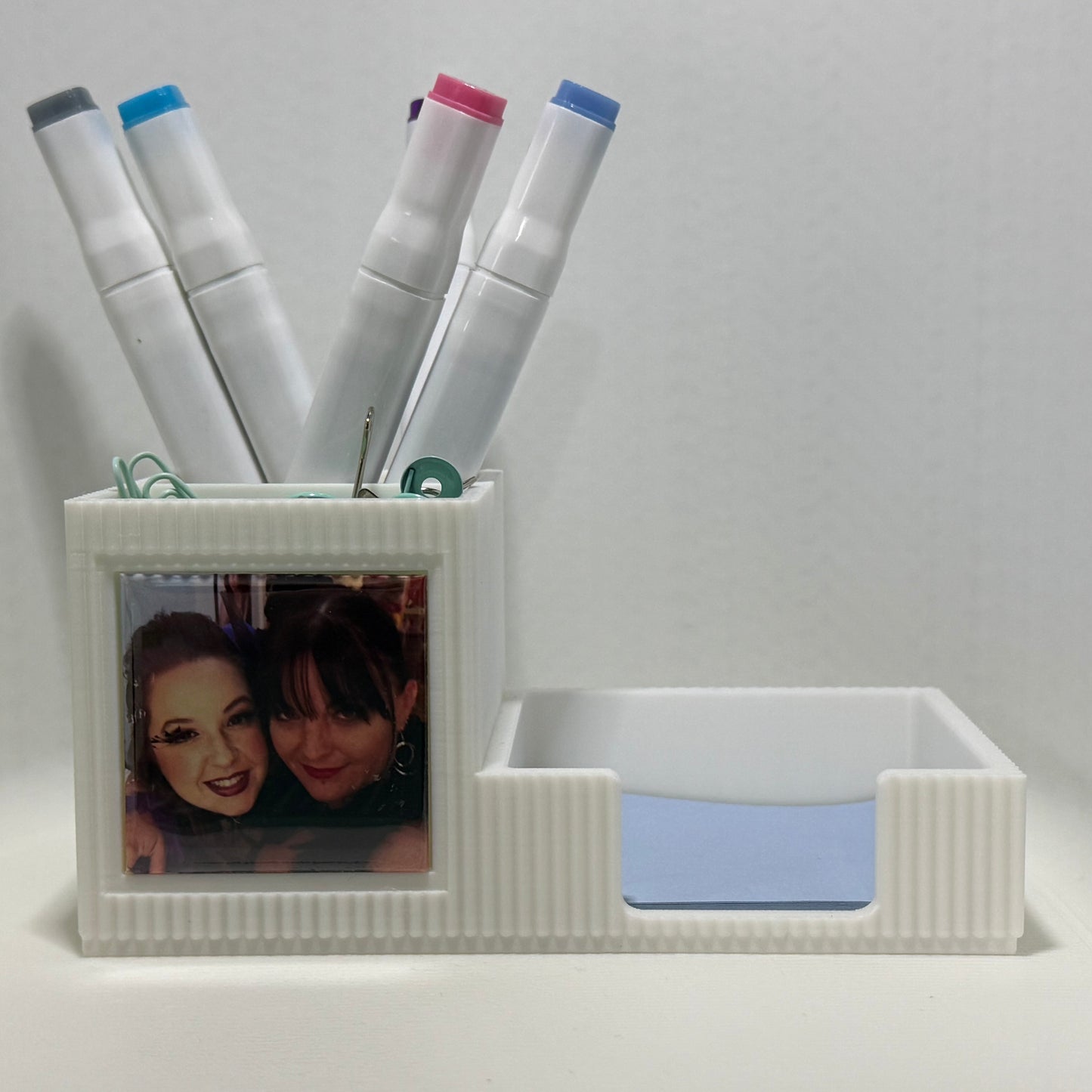 White desk organizer with markers and a photo frame on a white background
